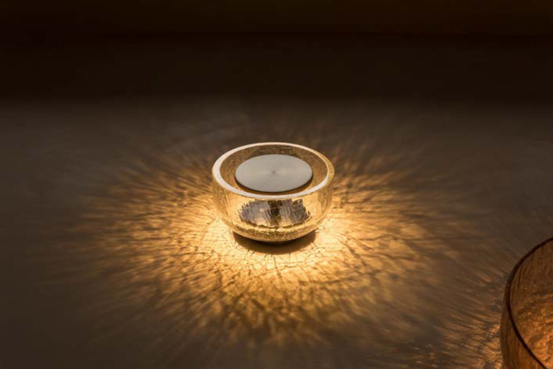 A lit candle in a glass bowl sits on a wooden table
